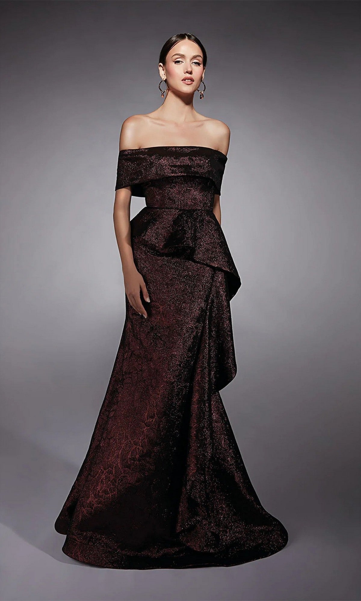 A woman poses against a plain gray background in the Alyce 27707 long formal dress, a burgundy fit-and-flare jacquard gown with an off-the-shoulder neckline, peplum detail, and flared skirt—perfect for a mother-of-the-bride.